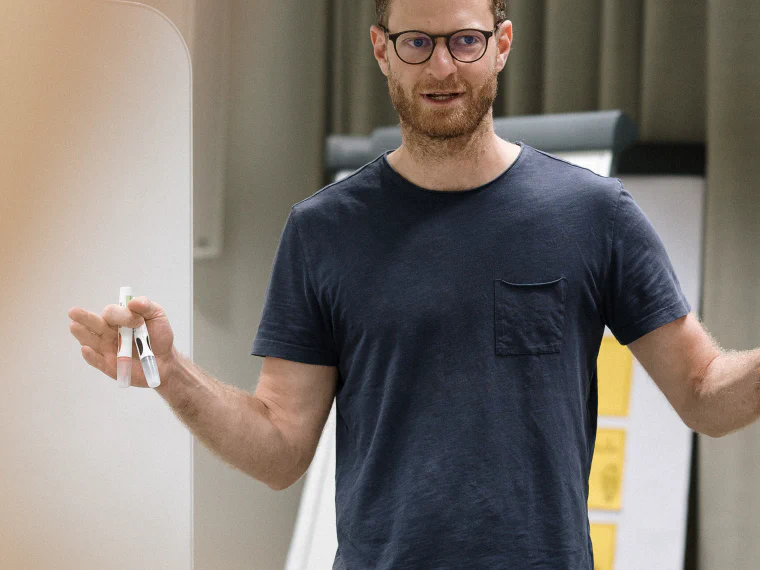 Basti stehend am Flipchart, Stift in der Hand, mitten im Satz